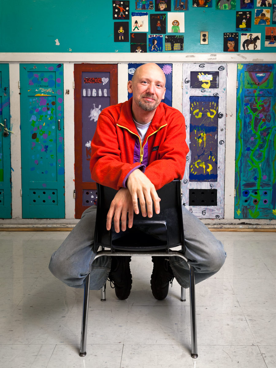 Morgan Jones Phillips sits on a chair in a classroom at Alpha Alternative School in front of a row of colourful painted lockers