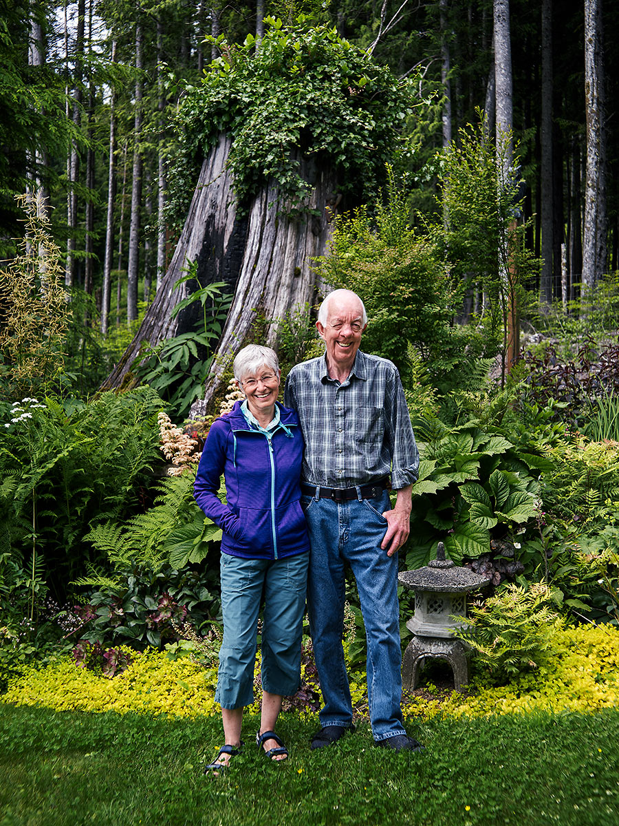 Shirley and Vern Sampson stand in front of an old growth cedar stump in their garden in Rough Bay, Sointula, British Columbia.
