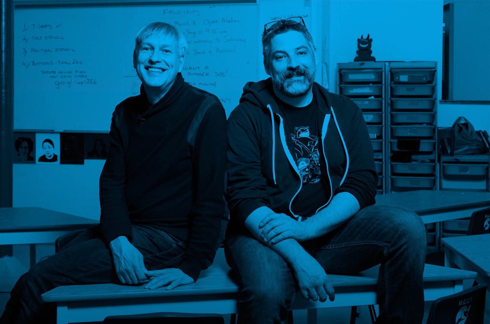 Triangle Program teachers Jeffrey White and Anthony Grandy sitting on a table in a classroom