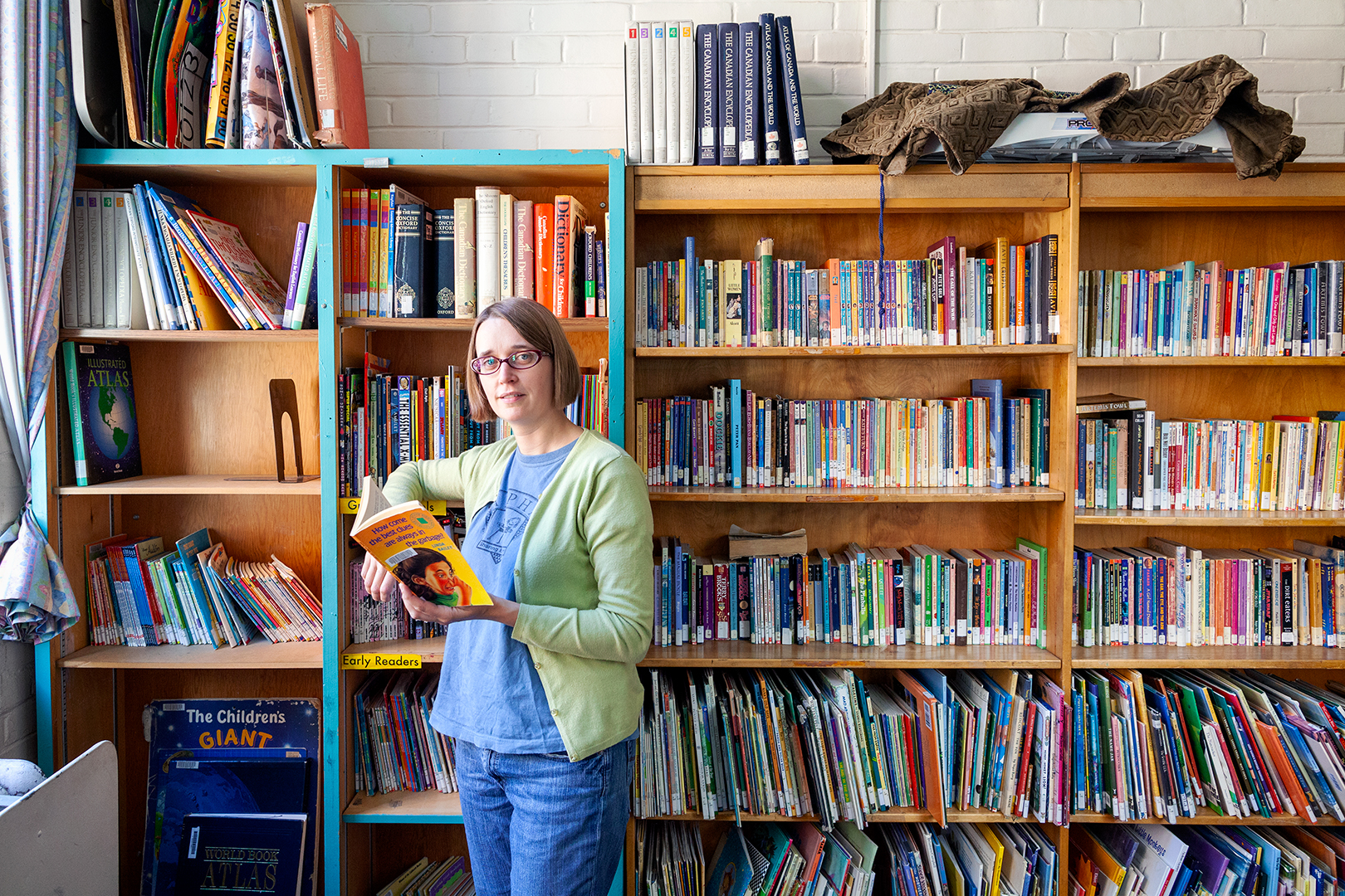 Maggie Marrelli stands with a book in hand in the library at Alpha Alternative School