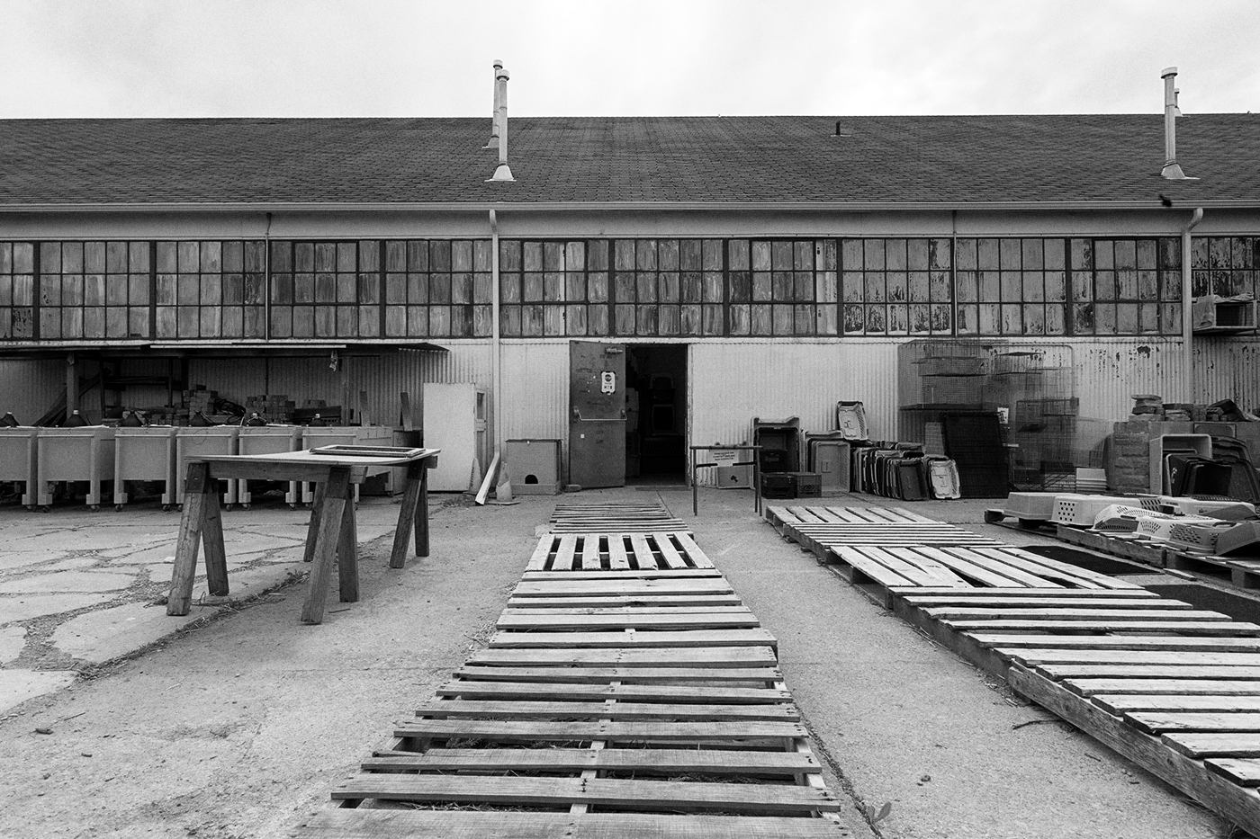 A large yard in front of low building, there are many wooden pallets in the yard.