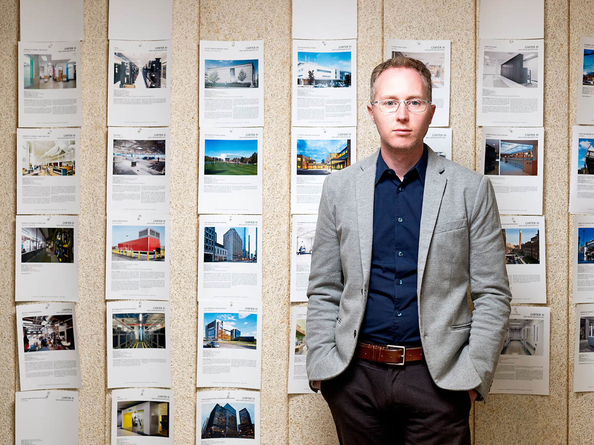 Alan stands in front of wall of paperwork at David Carter Architects