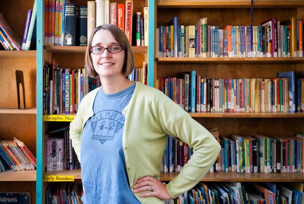 Maggie Marelli stands in front of book shelves at Alpha Alternative School