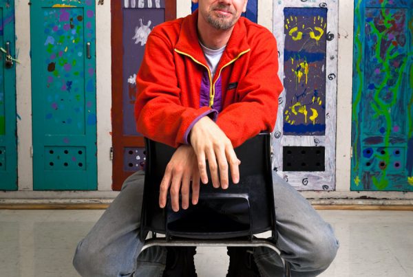 Morgan Jones Phillips sits on a chair in a classroom at Alpha Alternative School in front of a row of colourful painted lockers
