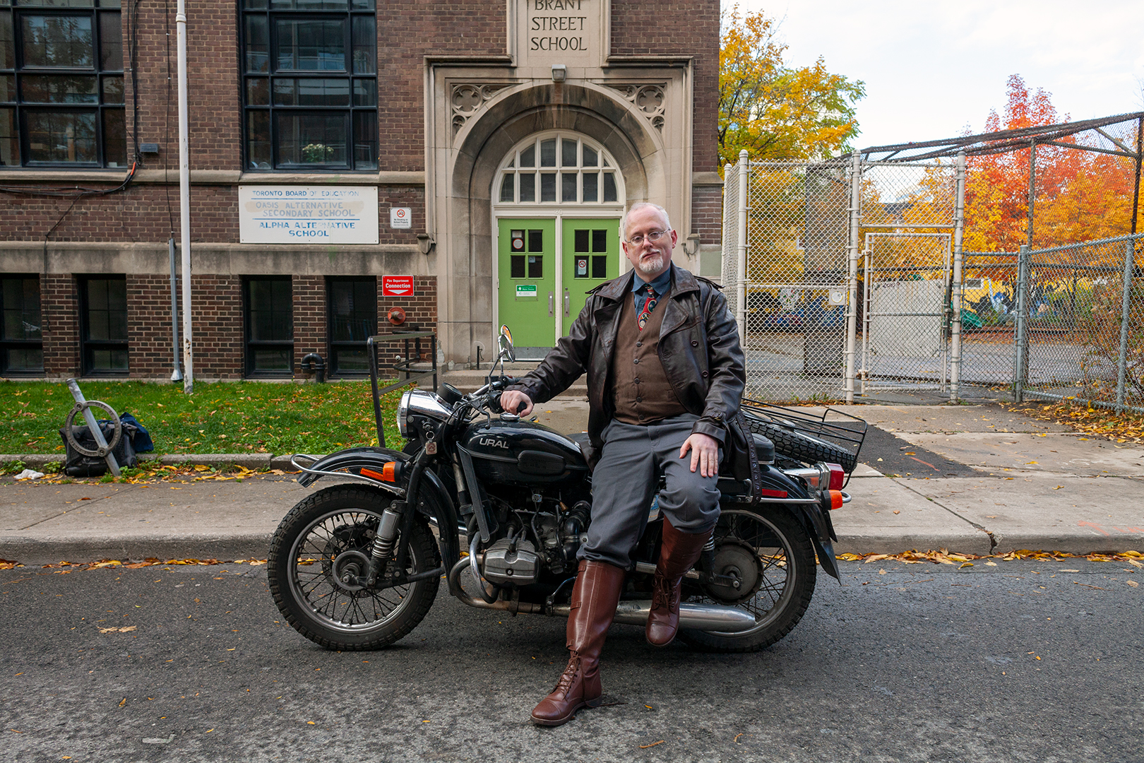 Jamie Leonard sits on a Ural motorcycle in front of Alpha Alternative School